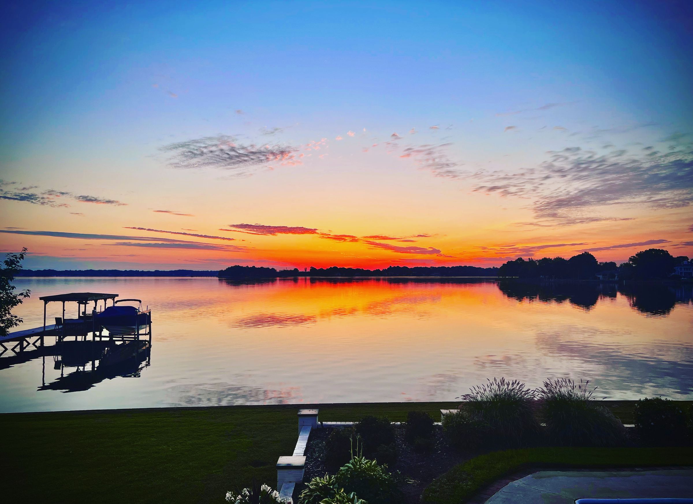 Sunrise over Lake Norman, a boat dock reflected in still water under a blue sky turning gold at the horizon