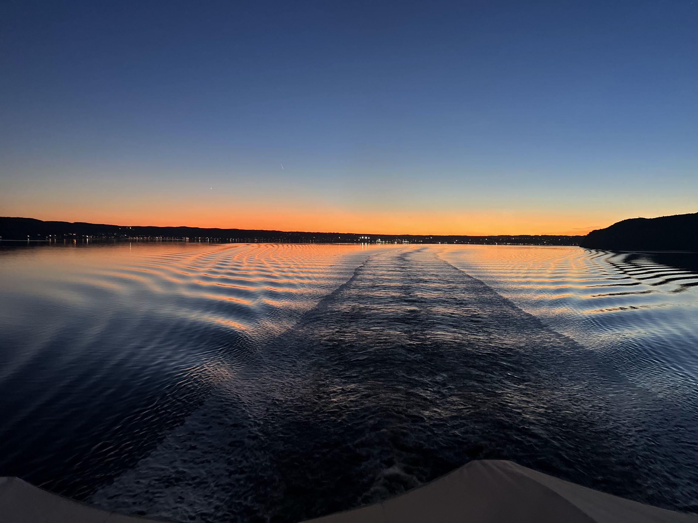 A boat's wake stretching across the lake toward an orange horizon at dawn